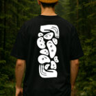 Hombre de espaldas usando playera de escalada Totem Holds negra con gráfico grande de tótem de holds en la espalda, en exterior.