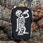 Playera negra de escalada Calaca escaladora colgada frente a una pared de roca con diseño de esqueleto escalador bebiendo agua.