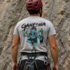 Escalador de espaldas con casco rojo usando playera Ganesha gris de Belay Partners en zona de escalada